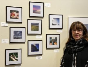 The image shows Sandy Brown Jensen with her exhibit at the opening of the PhotoZone Dec. 2019 show